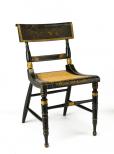 Chairs are ebonized with gold stencils and cane seats. The back has a scene of two figures on horseback, with left arms raising in greeting to a man with a walking stick. A home is in the distance with stairs in front and trees and hills behind. The lower back rail has stencils of stylized leaves. The front of the seat also has stenciled pattern.