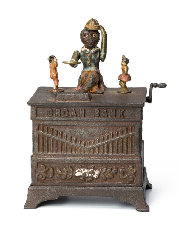 A mechanized coin bank. A figures sits holding a paddle on which a coin is placed. When the handle is turned the paddle is dropped, the hat is doffed, and two small children dance on either side.