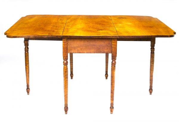 A drop leaf table, known as a gate-leg for the extra leg that swings out two sides to support the drop leaves. The table is made of tiger maple with spindle legs and blunt arrow feet .
