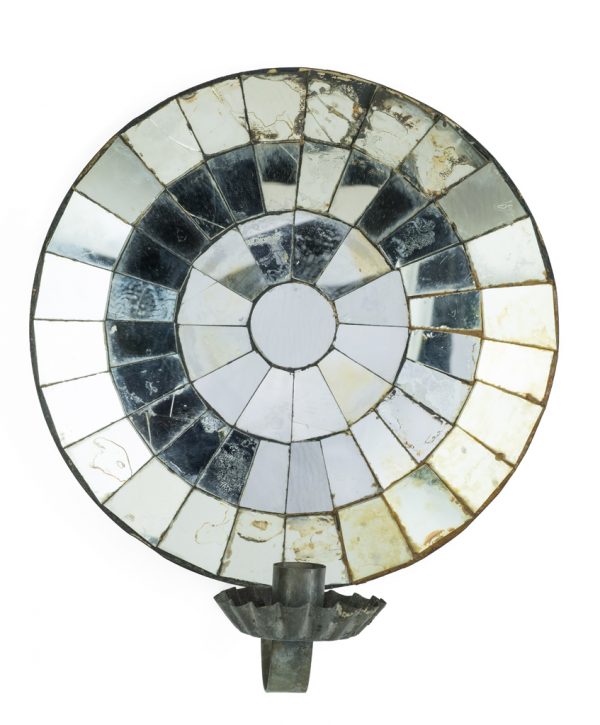 A mirrored sconce made primarily of ferrous metal that is plated or galvanized. The backing is circular and concave, lined with mirrored glass pieces. A candle cup and bobeche are attached to an arm that is extended from the bottom edge.