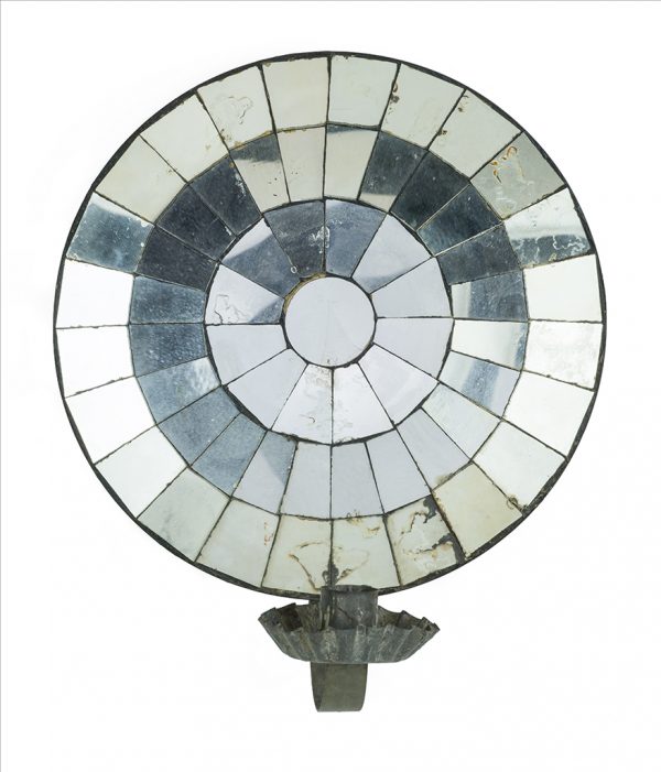 A mirrored sconce made primarily of ferrous metal that is plated or galvanized. The backing is circular and concave, lined with mirrored glass pieces. A candle cup and bobeche are attached to an arm that is extended from the bottom edge.