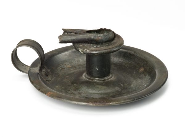 A hogscrapper candlesick holder with short center, loop handle, and a clip to hold the candle.