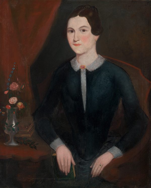 A woman sits with her hands in her lap, a vase of flowers is to her left. She wears a black  dress with a lace collar.
