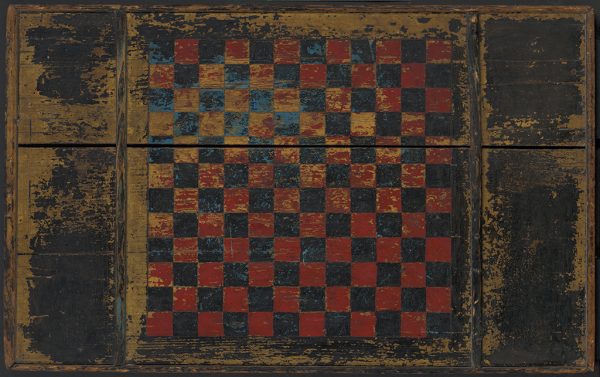A red and black and blue checkerboard with black extentions on the sides. On the back of the board is an uncompleted game carving.