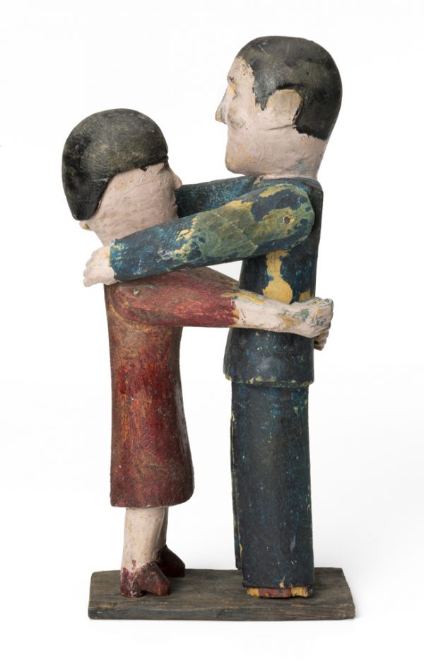 A dancing couple. She is in a red dress with her arms around his waist. He is in a dark gray suit with his arms on her shoulders.