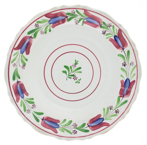 A shallow bowl with wide, flared rim. The ceramic body is white and opaque with a low degree of vitrification, possibly earthenware. There is a floral design on the rim and concentric circles in the bottom of the bowl surrounding a small foliate design in red, blue and green.