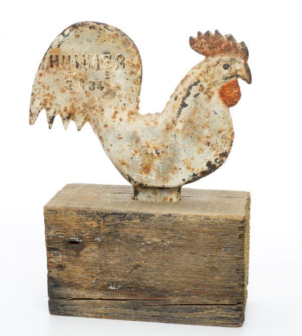 A windmill weight of a white rooster, with red cock and comb. The rooster is mounted to a wood base.