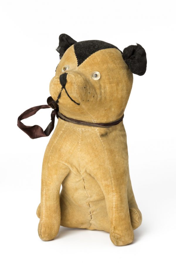 Sitting dog with black ears and ribbon collar. When you press his tummy it squeaks. He has plastic eyes and embroildered nose and mouth.