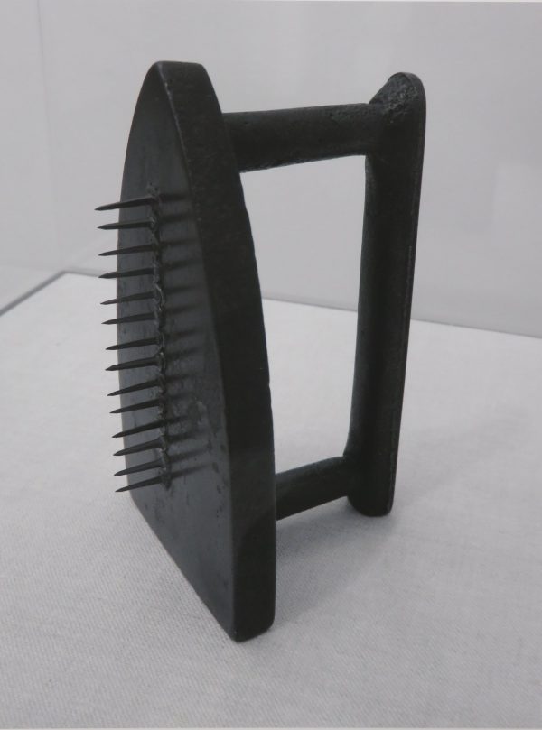 Photo of a iron, with nails projecting in a row, down the center.