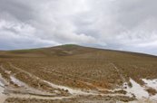 A barren mountain with snow in the ruts in the foreground.