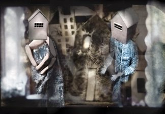 Two puppet figures, with houses for heads, are in front of more houses, with decorative surfaces. Two white shapes along each side add to the dream-like presentation.