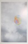 A single soap bubble is framed by a cloudy sky with the sun peaking throught the clouds at the top right corner. The bubble has a rainbow of colors