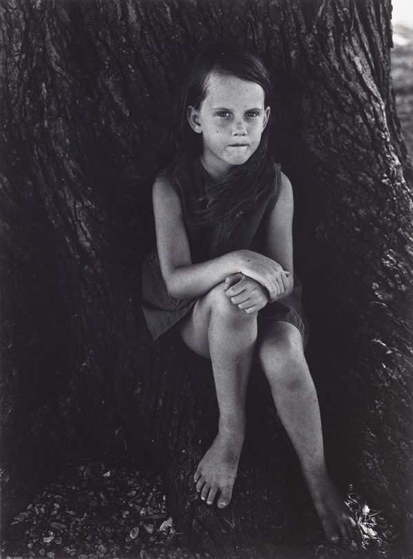 Young girl sits at the base of a tree.