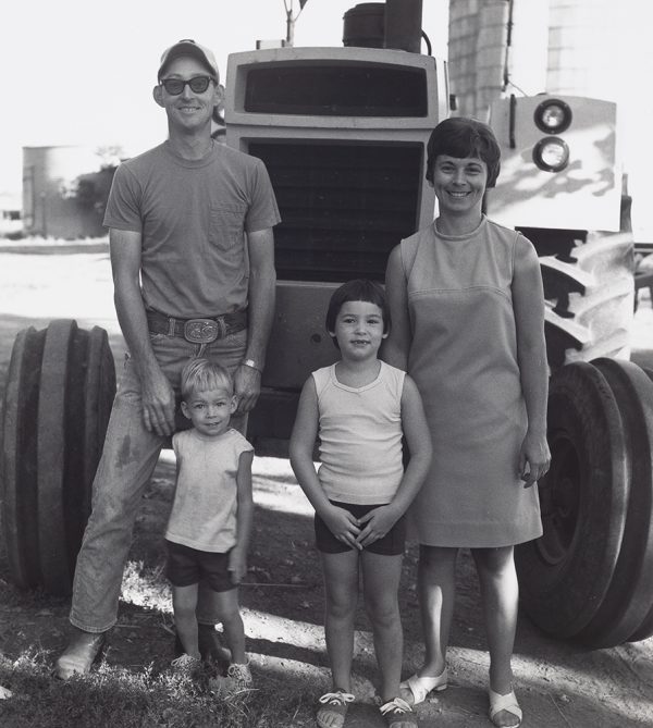 A young couple and two young boys pose in front of a tractor.