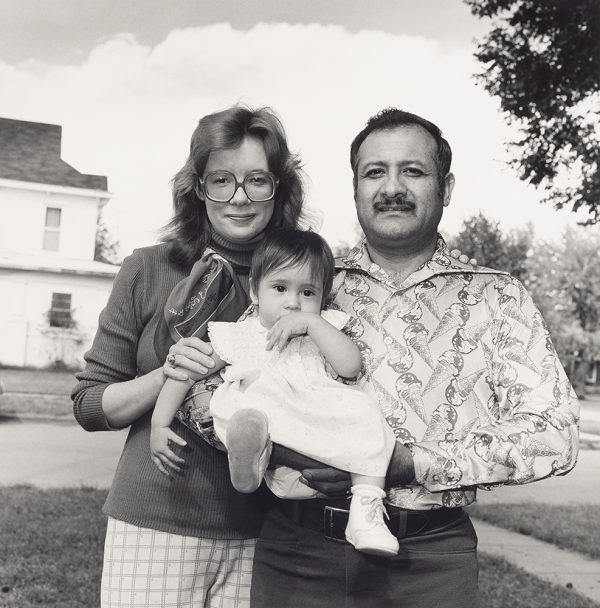 A young couple poses together holding their child between them.