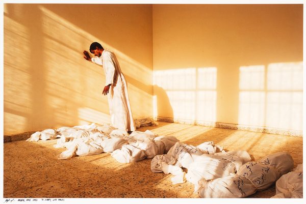 Man stands leaning against wall over dead bodies in cloth bag with identification written on them. Al-Mahawil (????????) is a district in Babil Governorate, Iraq