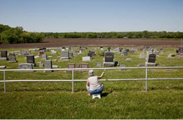 A woman sits painting a fence around a rural cemetery.
