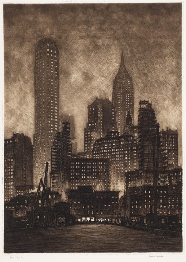 An empty street leads up to a tall skyline of dark buildings with lights in each window.