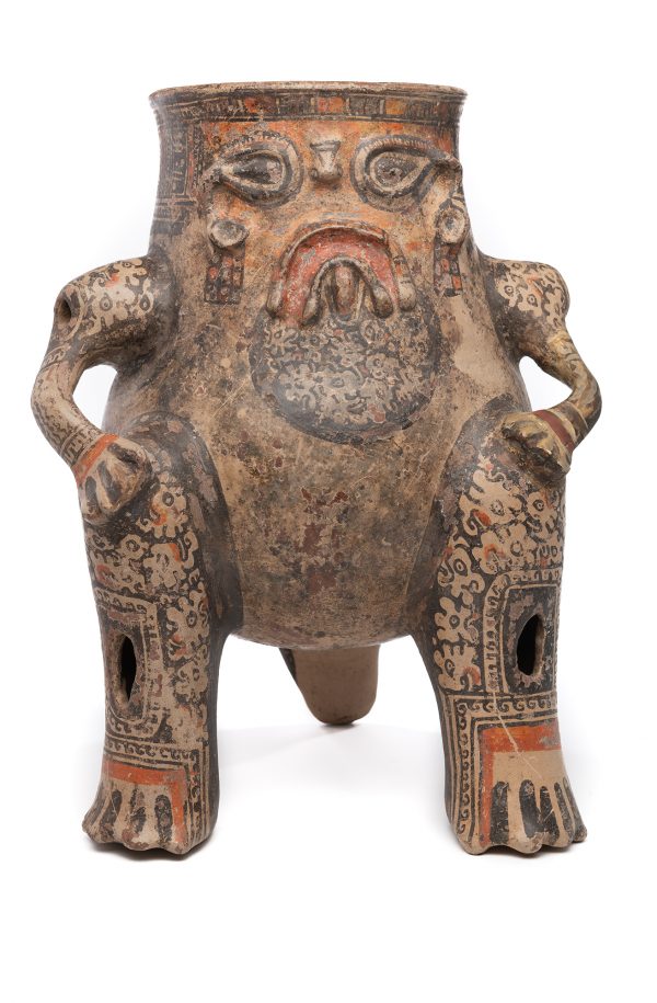 Jar is in rust color clay with creajm ground, black and rust color decoration. A tripod using two front legs and jaguar tail as the third leg. The projecting arms have shoulders with holes and the hands have four fingers reasing on hips. The face is human like, with tear drop eyes, and a tiny nose, frowning mouth. The design on the arms, legs and tail are also jaguar or flower like. The top frieze around the rim is a decorative geometric design. This pot is a rattle.