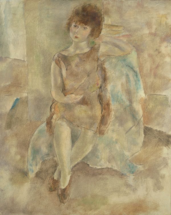A woman sits on a cloth covered chair with her right arm in her lap and her left arm resting on the back of the chair.