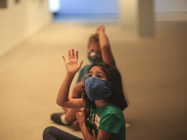 Interior image of kids wearing masks and sitting on the fllor of the galleries