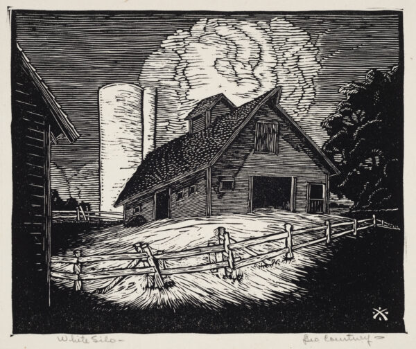 A white grain silo is attached to a barn with an open door. Behind are clouds and in front is a split rail fence.