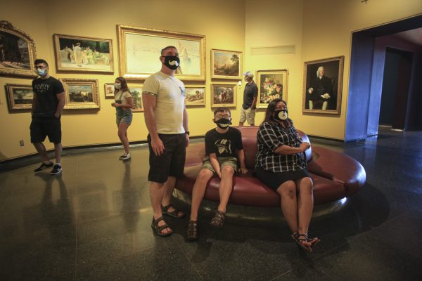 Visitors in the Rotunda Gallery sitting on a round ottoman and looking at paintings on the wall