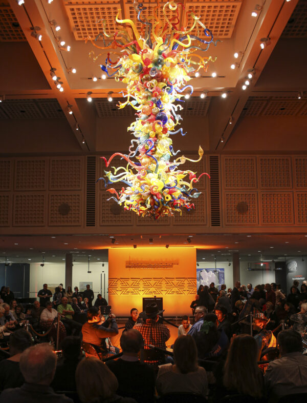 Photo of the Chihuly Chandelier at night with people sitting at tables and chairs underneath it