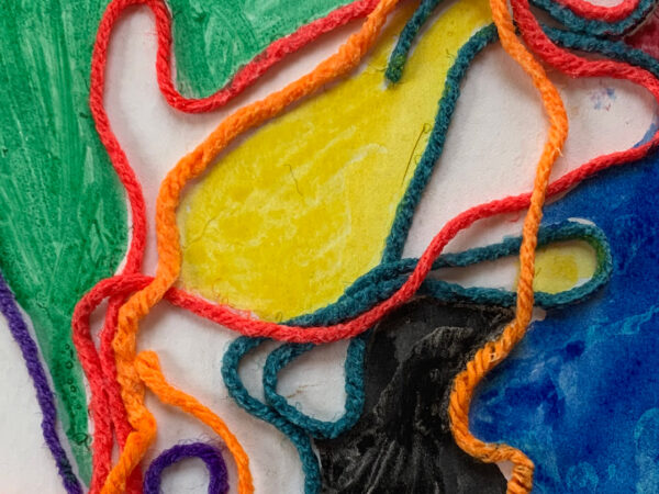 Photo of colorful yarn in orange and red with yellow, green and white colors behind