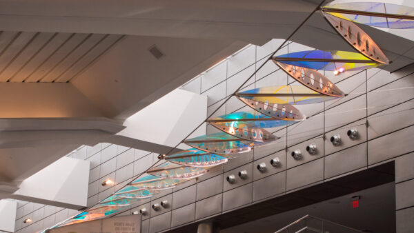 Interior photo of Wichita's Eisenhower Airport with a large-scale multicolored artwork hanging in sections from the ceiling over an escalator