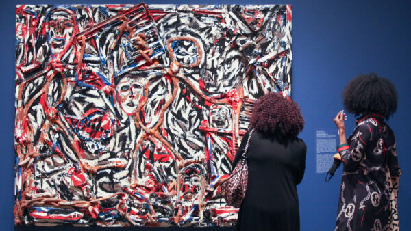 Two women with their backs towards the camera look at an abstract painting against a blue gallery wall