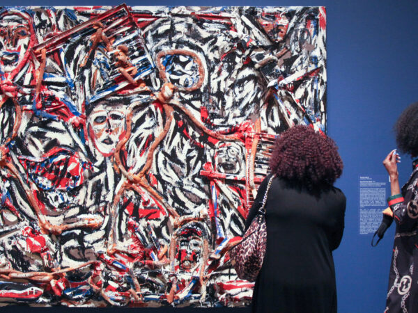 Two women with their backs towards the camera look at an abstract painting against a blue gallery wall