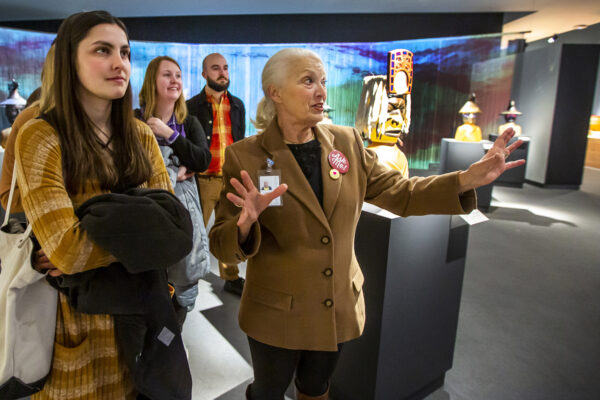 Several people in a gallery, Young woman in the foreground with long brown hair and carrying a coat. Older woman with a red