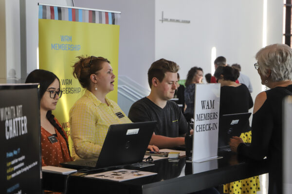 Three museum staffers standing behind a table and checking in event attendees using laptops