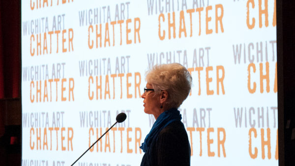 Photo of a woman in shadow standing in front of a projection screen in the darkened Howard E. Wooden Lecture Hall with the words Art Chatter projected onto the screen