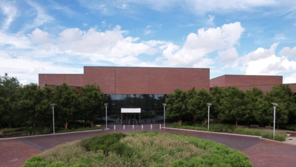 Photo of WAM's main entrance with tall doors and glass windows while showing the circular red brick drive, green plantings in front and trees on either side