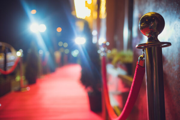 A red velvet rope hangs from a gold stanchion with a red carpet out-of-focus and off to the left side of the frame