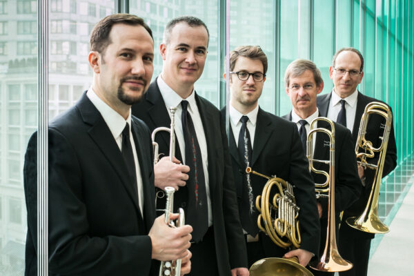 Five men dressed in dark suits, each holding a brass musical instrument