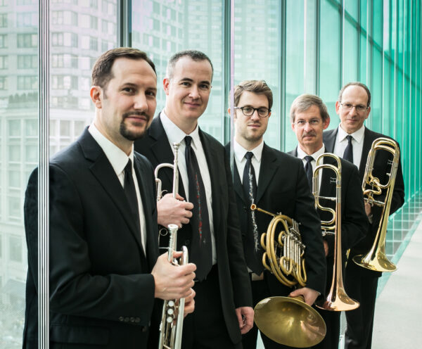Five men dressed in dark suits, each holding a brass musical instrument