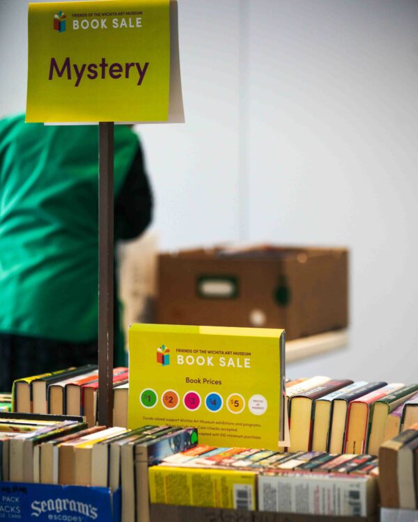 Boxes of books on a table, with a sign just above the books with pricing by colored dot and a sign with the word Mystery on a rod about 12 inches above the books