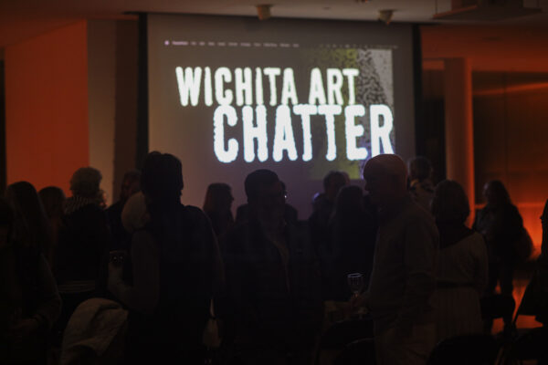 People silhoutted against background of a screen with Wichita Art Chatter displayed