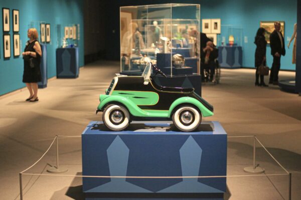 Gallery picture with a 1930s green and black pedal car on a two-tone blue pedestal