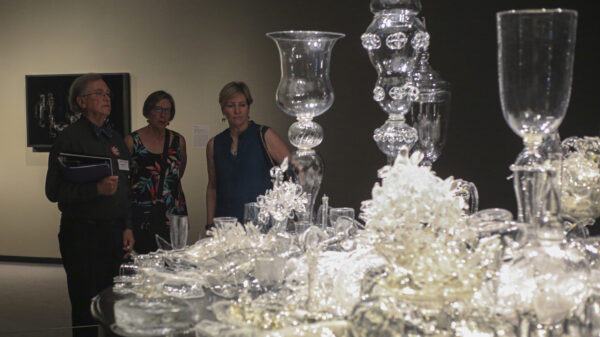Man and two women looking at a glass sculpture