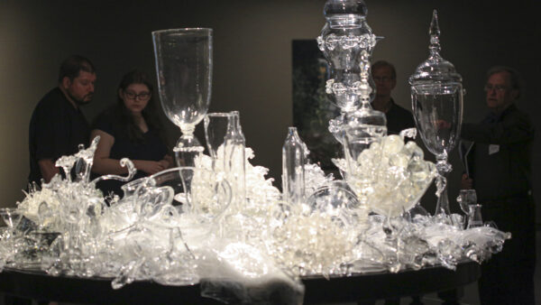 Clear glass sculpture of a table top covered with vases, bowls, and other glass