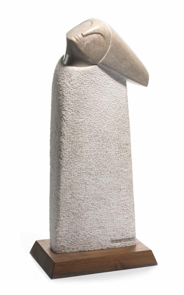 Sculpture of an elongated head of brown stone, placed at an angle on a pedastal of a pebble-textured material in off-white