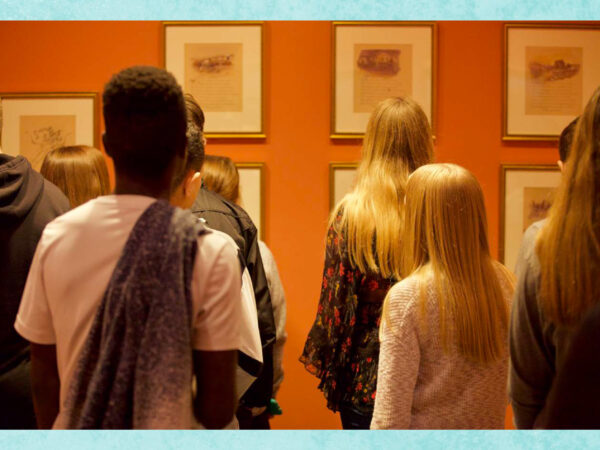 Group of six middle school students with their backs to the camera looking at art on an orange wall in the galleries