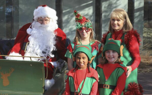 Three children and an adults, dressed in red and green elf outfits, standing next to Santa Clause