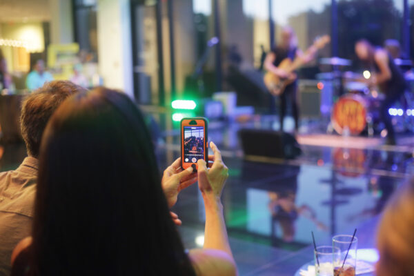 Person holding a cell phone taking a photograph of a band playing.