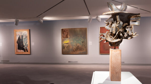 Gallery image with a metal sculpture in the foreground and three paintings in the backgroun