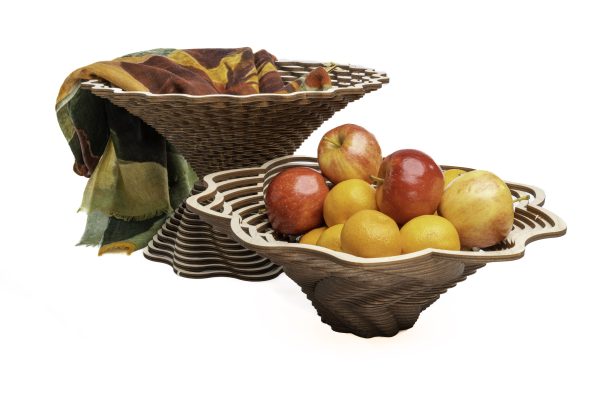 Wooden baskets, one with red apples and oranges in front of a taller basket with a piece of cloth in grees, yellows, oranges, and browns spilling from the top